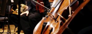 Musician rests his cello on stage surrounded by the rest of the symphony orchestra.