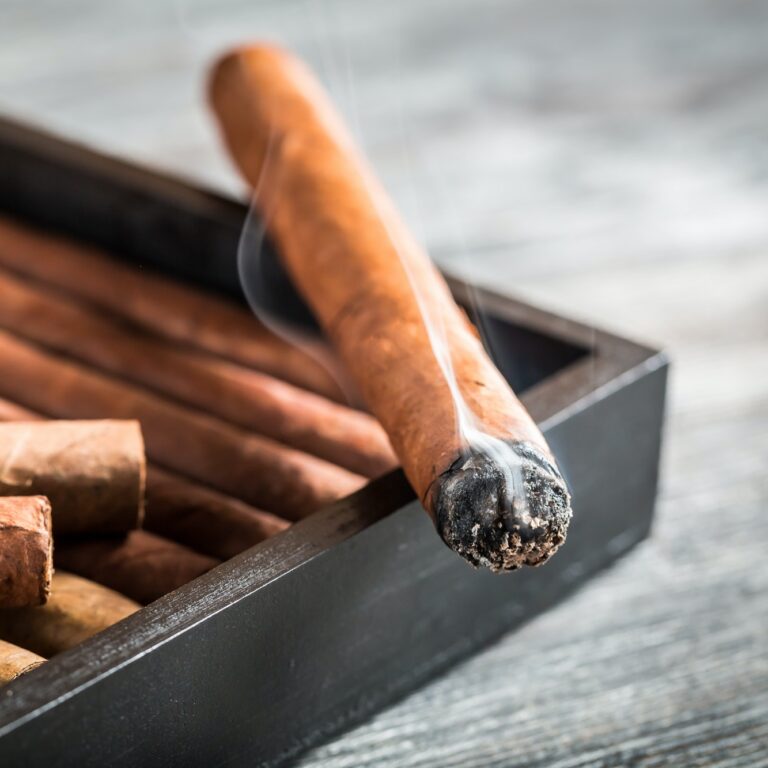 Burning cigar with smoke on wooden humidor