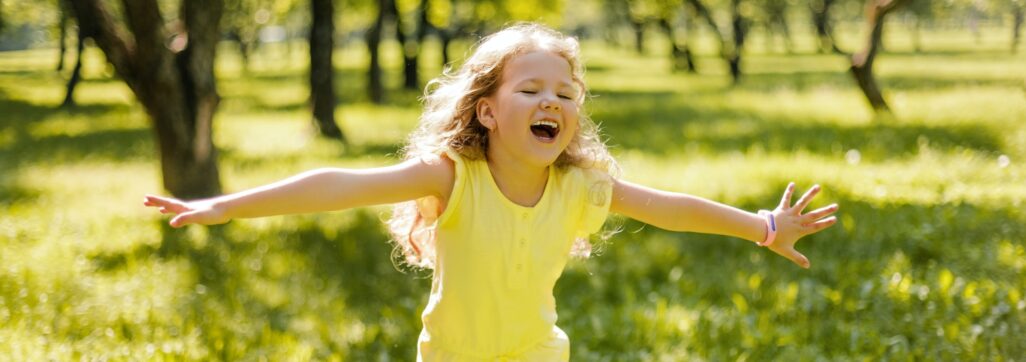 A happy child playing in a summer park. The girl is running, spinning, spinning and laughing