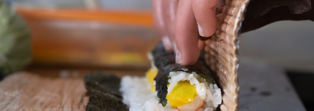 Hands of unrecognizable person making sushi rolls with bamboo mat