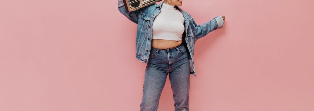 Happy girl in denim wide jacket and tight pants posing on pink background. Stylish woman in white s