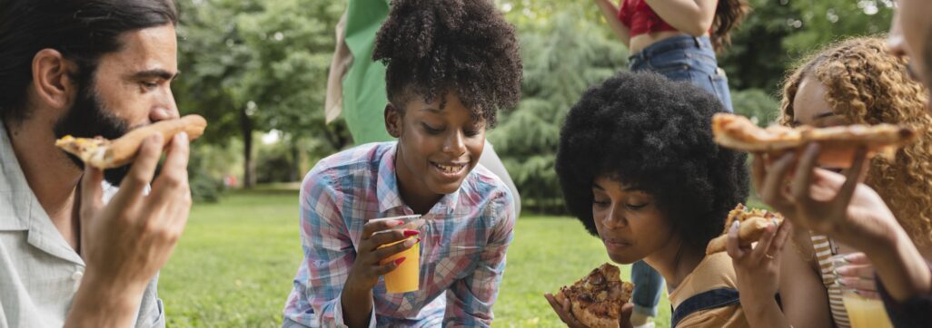 multiracial friends enjoying a party outdoors in the park while eating pizza
