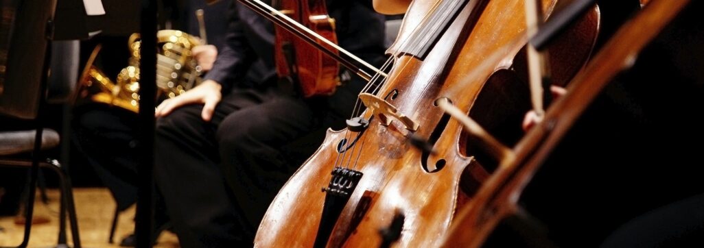 Musician rests his cello on stage surrounded by the rest of the symphony orchestra.