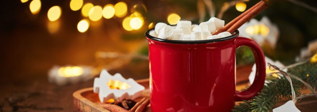 Red cup of hot cocoa with marshmallows and glowing garland for christmas