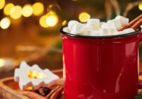 Red cup of hot cocoa with marshmallows and glowing garland for christmas
