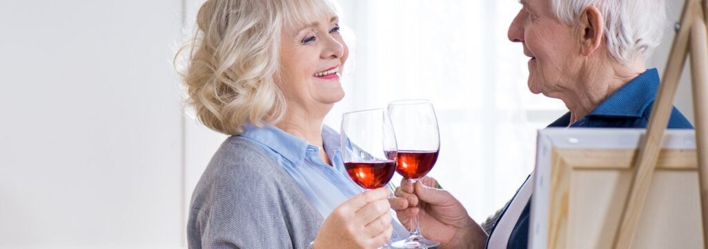 side view of smiling senior couple drinking wine in art workshop