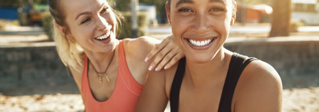 Two women laughing while taking a break from exercising outside