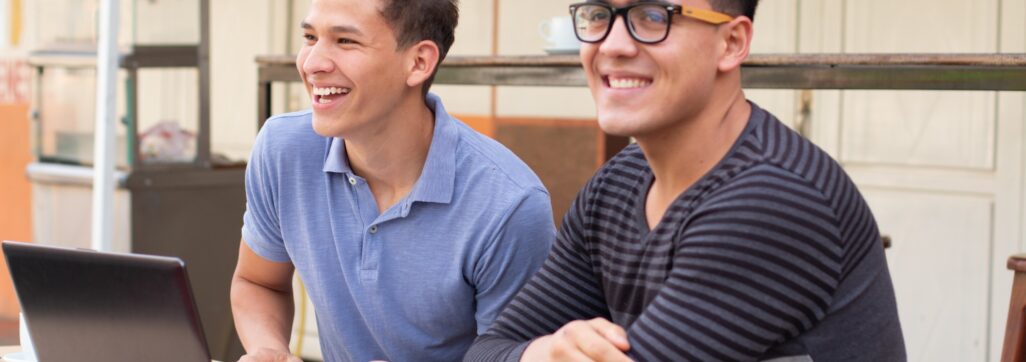 Two young adults laughing. Students at desk outdoors.